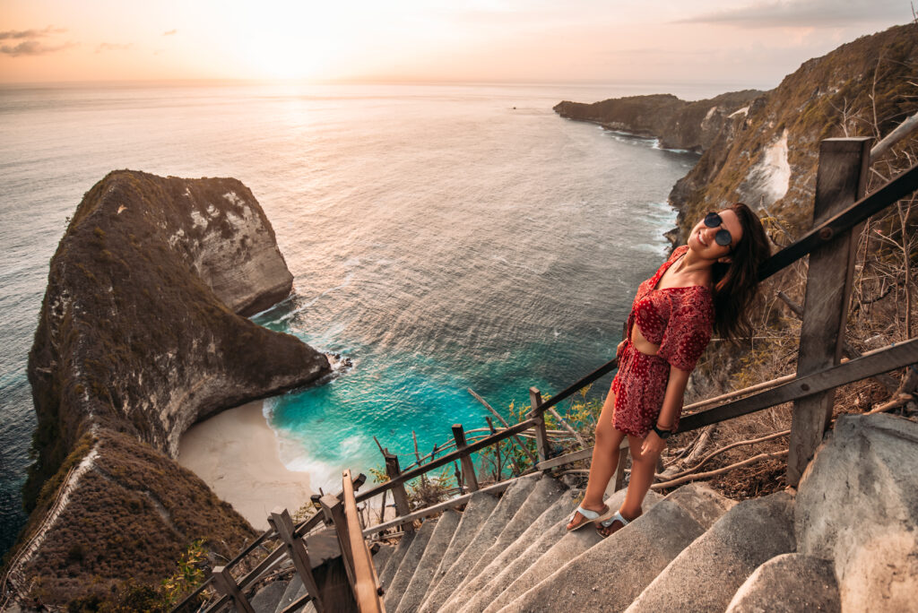 Mujer posando en las escaleras del mirador de la playa de Kelingking, Nusa Penida, al atardecer