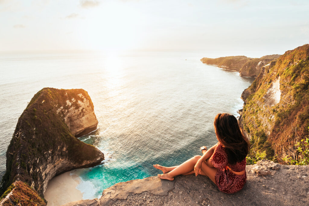 Mujer sentada en el mirador de la playa de Kelingking con los acantilados de T-Rex en Nusa Penida al atardecer
