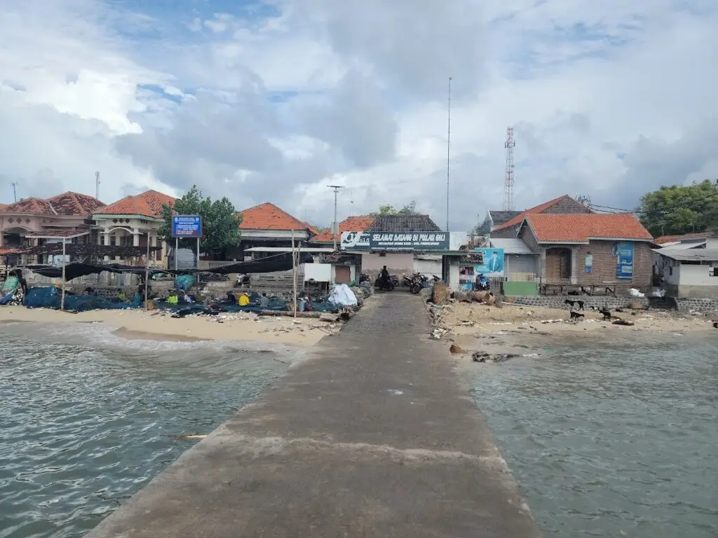 Vista de la playa de Gili Ketapang con barcos de pesca y edificios locales. "Bienvenido a la isla Gili