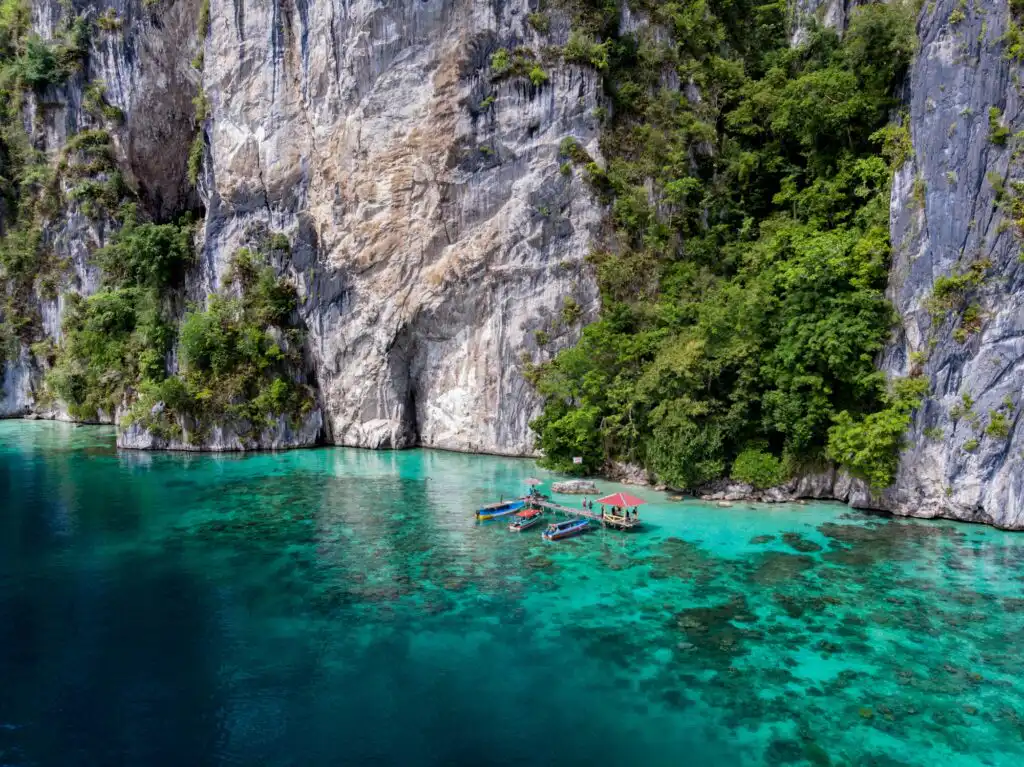 Een luchtfoto van een boot op Ora Beach, Maluku. Turquoise water en indrukwekkende kalkstenen kliffen.