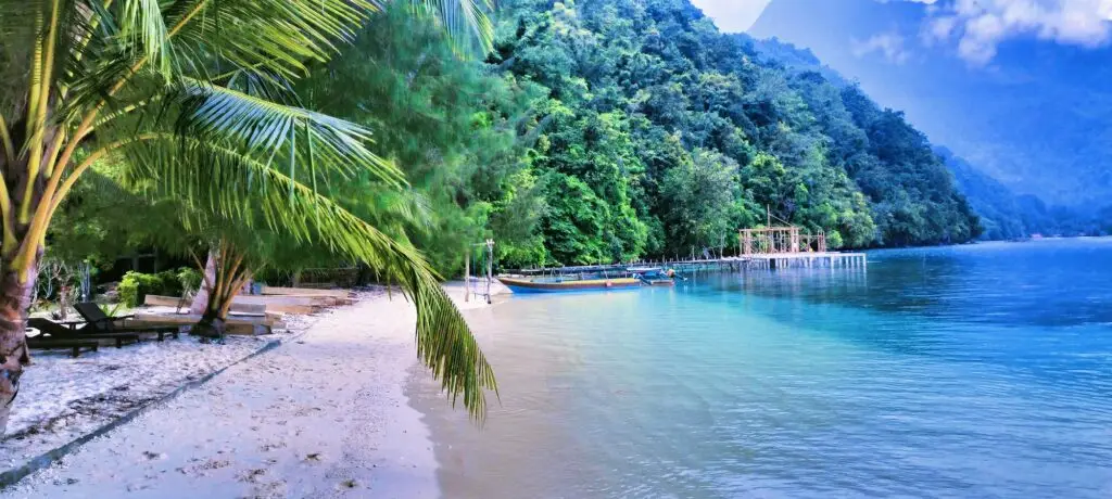 Het prachtige Ora Beach in Maluku, met kristalhelder water, wit zand, palmbomen en traditionele boten.