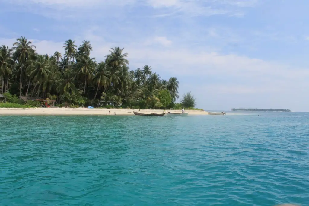 Pulau Banyak Aceh Singkil: Turquoise water meets white sandy beaches with palm trees and boats, a hidden paradise.
