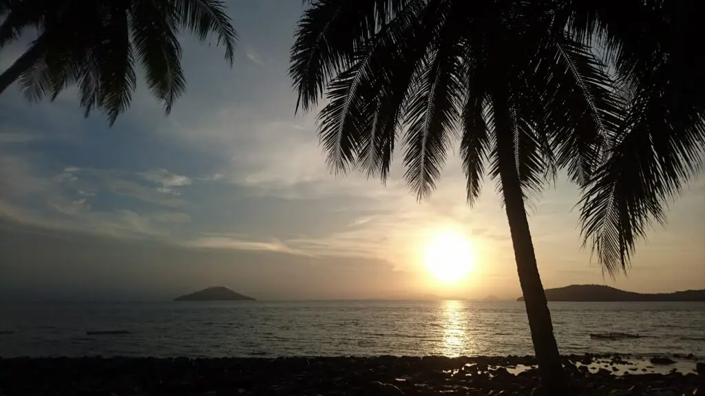 De zon gaat onder boven de zee op het eiland Lemukutan, West-Kalimantan, met palmbomen als silhouetten.