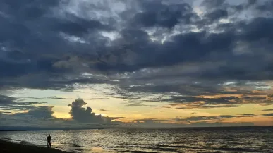 Een silhouet van een persoon in Nabire bij zonsondergang. Dramatische wolken boven de oceaan.