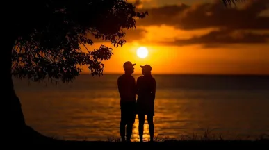 Een stel geniet van de zonsondergang op het strand. Een romantisch moment met de oranje lucht en de oceaan.
