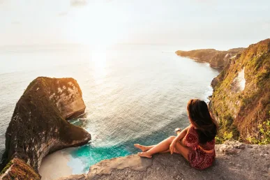 Vrouw zittend op uitkijkpunt Kelingking Beach met T-Rex kliffen in Nusa Penida bij zonsondergang