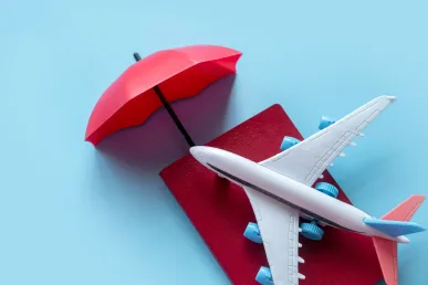 Bayi pesawat mainan di atas buku merah dan payung merah di latar belakang biru yang cerah, cocok untuk konten perjalanan dan wisata anak-anak.