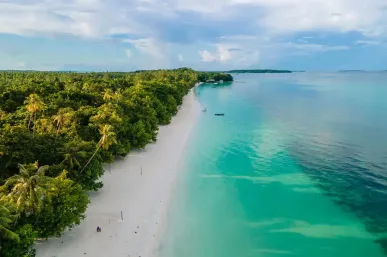 Een luchtfoto van Ngurbloat Beach met wit zand, turquoise water en palmbomen.